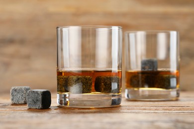 Whiskey stones and drink in glasses on wooden table, closeup