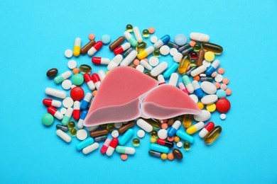 Paper liver and pills on light blue background, flat lay. Hepatitis treatment