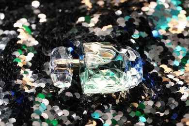 Photo of Luxury perfume in bottle on fabric with shiny sequins, closeup