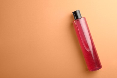 Photo of Bottle of pink cosmetic gel on pale orange background, top view. Space for text
