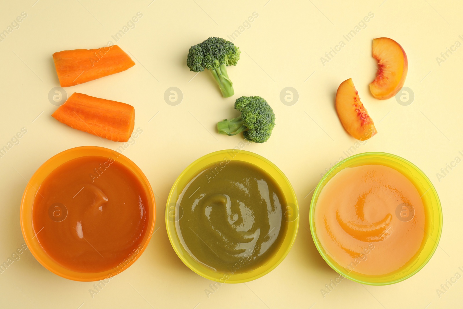 Photo of Baby food in bowls and fresh ingredients on yellow background, flat lay