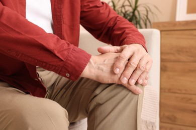 Senior man suffering from pain in his knee at home, closeup. Arthritis symptoms