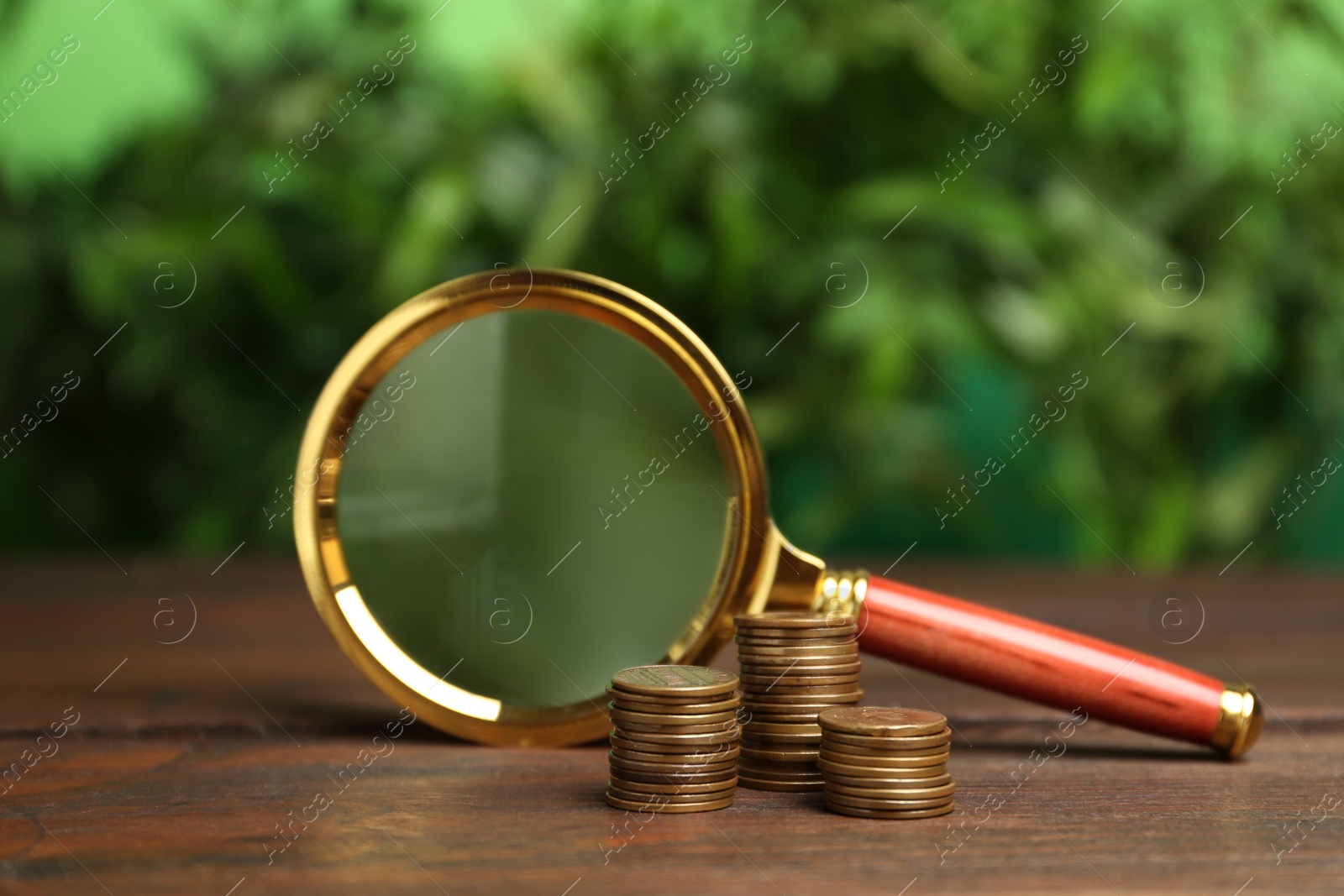 Photo of Coins and magnifying glass on wooden table against blurred background. Search concept