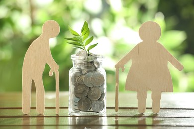 Pension savings. Figures of elderly people, coins and green twig in jar outdoors