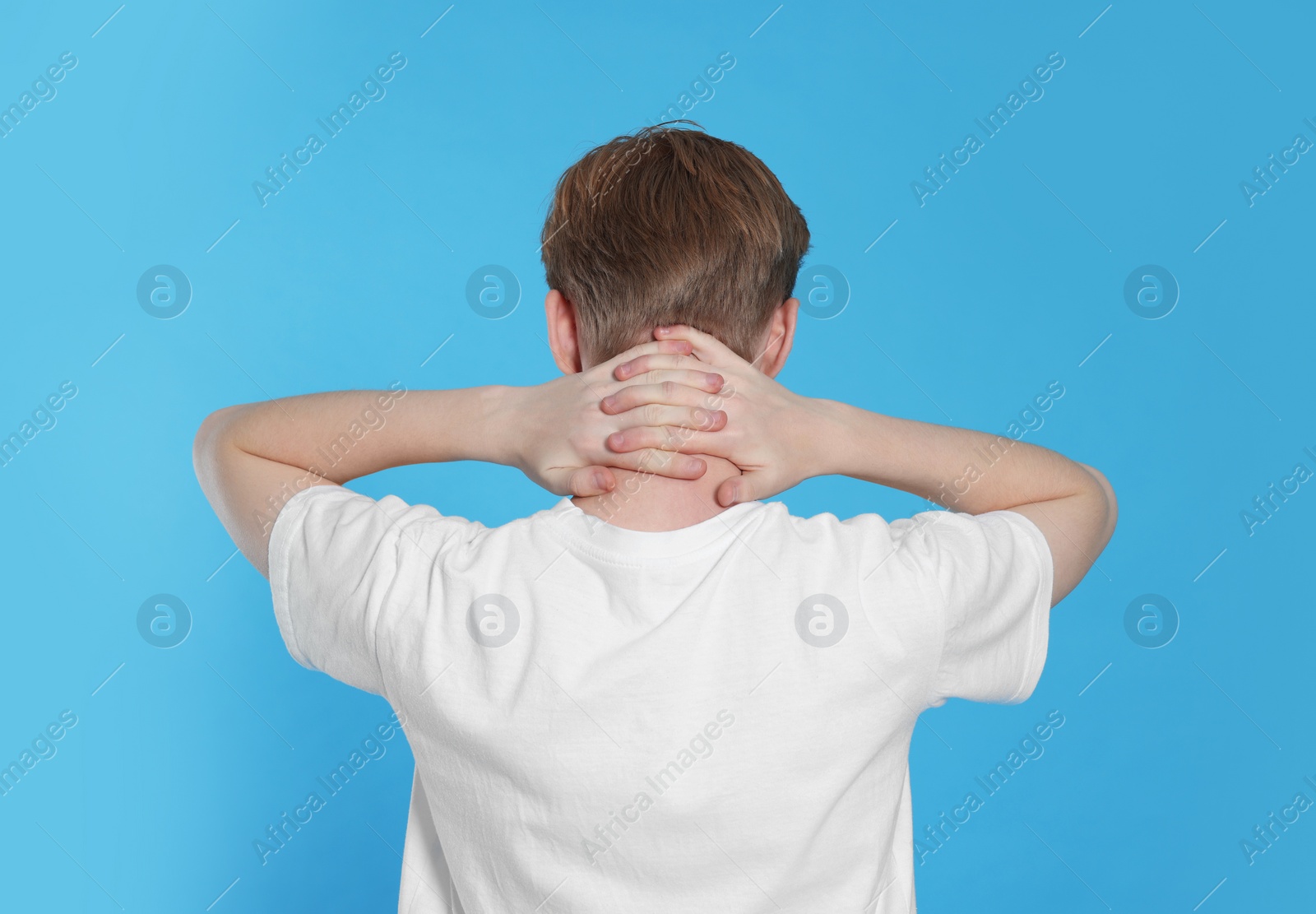 Photo of Teenage boy suffering from pain in neck on light blue background, back view. Arthritis symptom