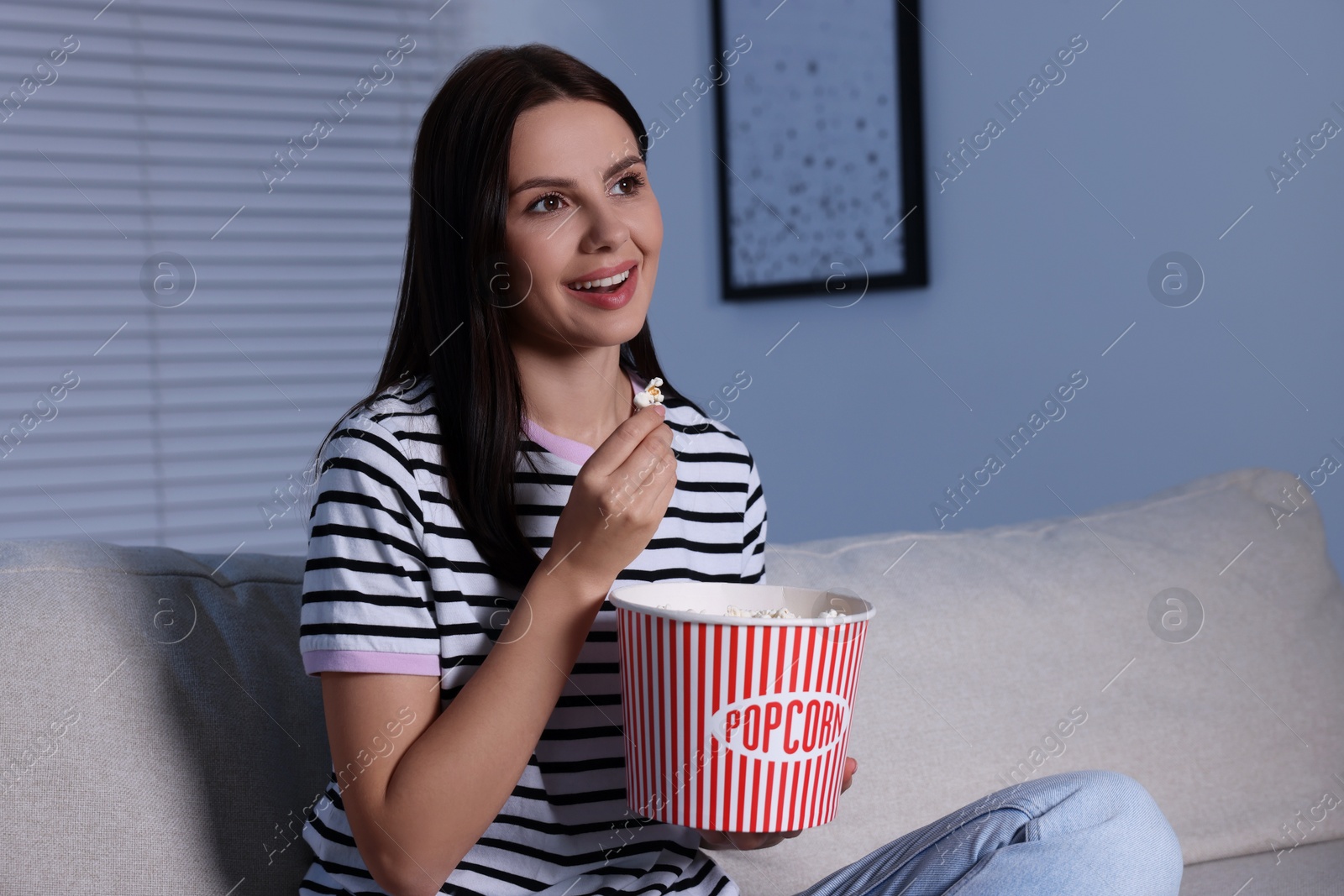 Photo of Happy woman eating popcorn while watching TV at home in evening