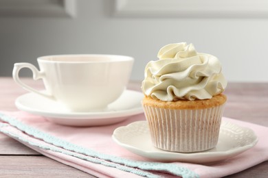 Photo of Tasty cupcake with vanilla cream on pink wooden table, closeup