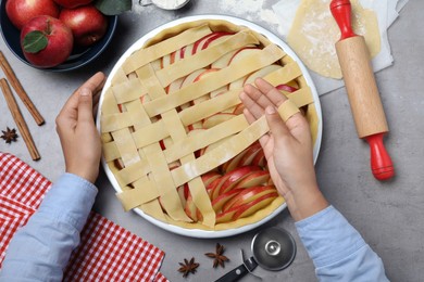 Photo of Woman decorating raw apple pie at grey table, top view