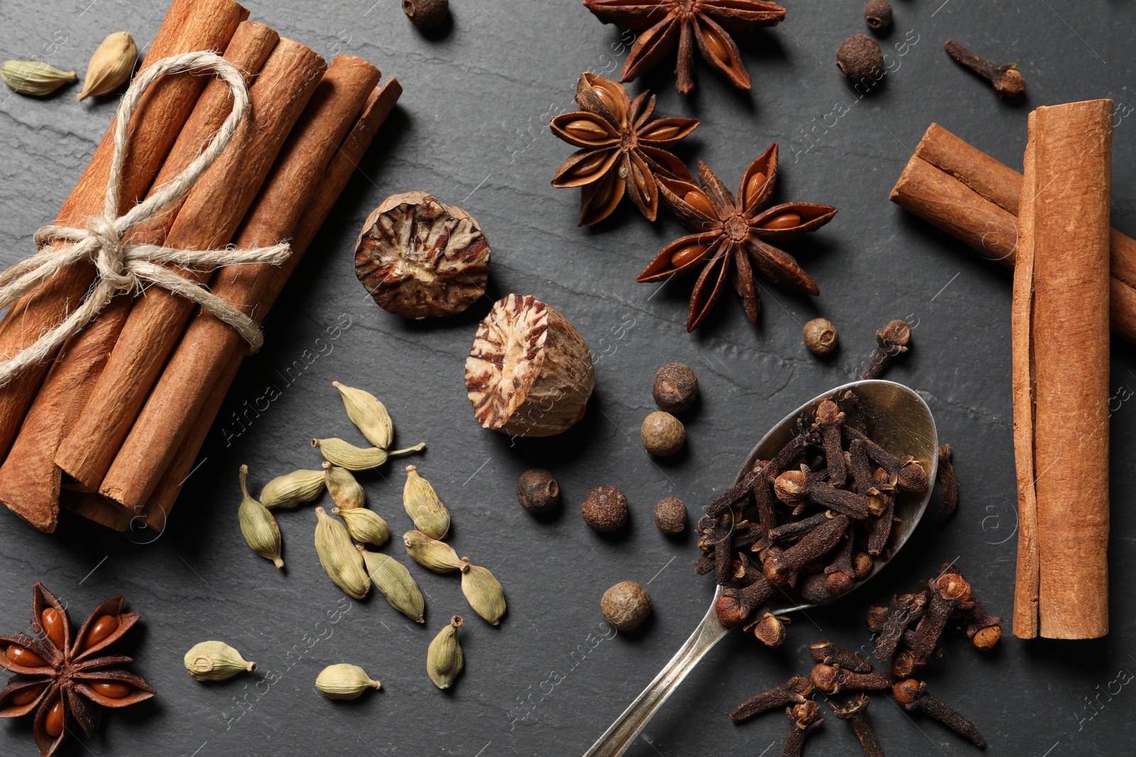 Photo of Different spices and spoon on dark gray textured table, flat lay