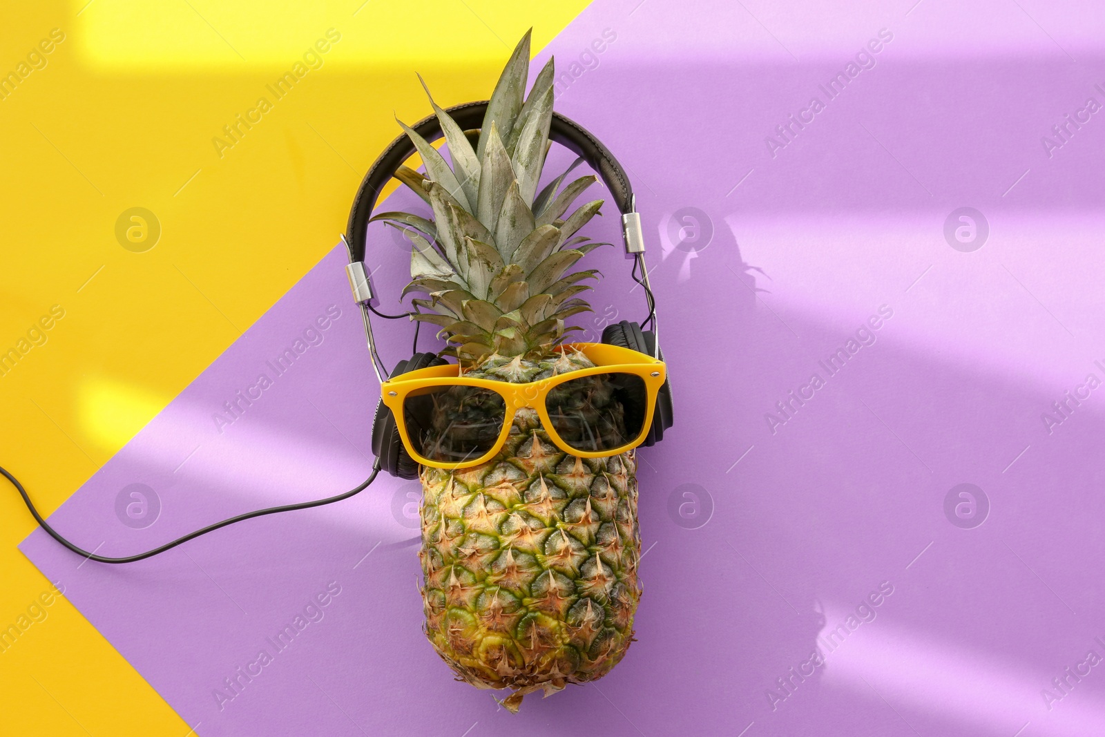 Photo of Fresh ripe pineapple with headphones and sunglasses on color background, top view