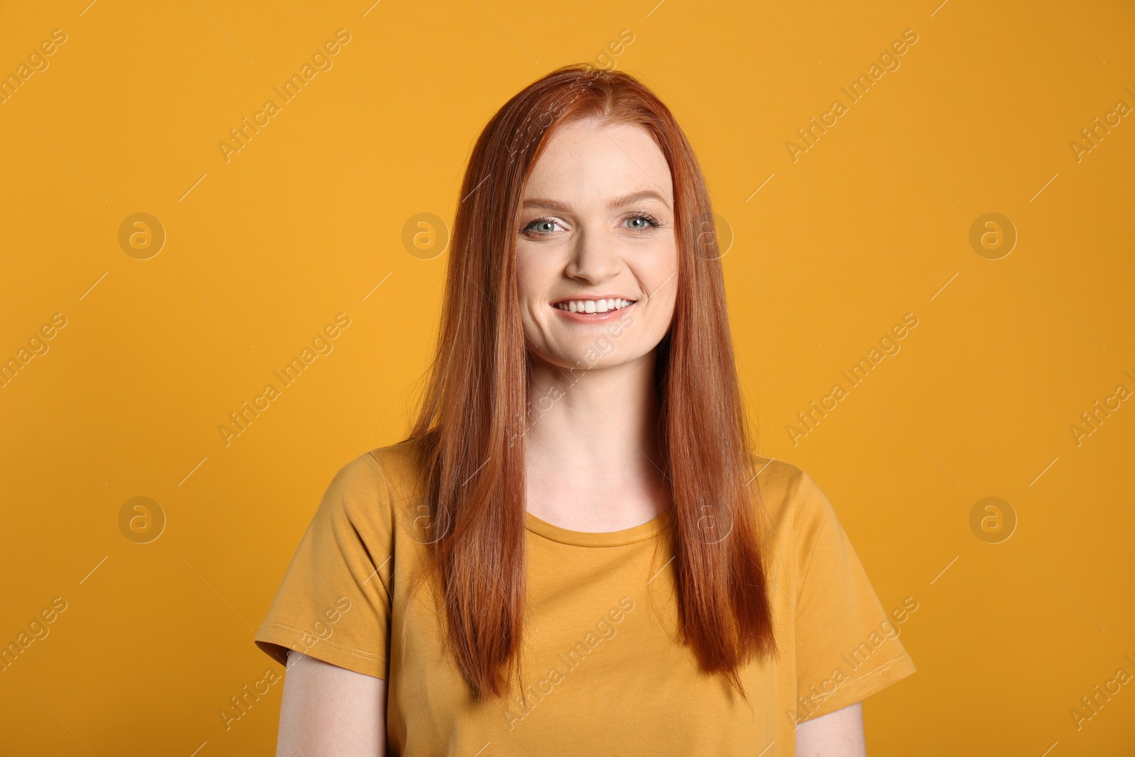 Photo of Candid portrait of happy young woman with charming smile and gorgeous red hair on yellow background