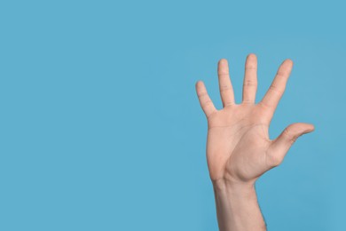Photo of Man giving high five on light blue background, closeup of hand. Space for text