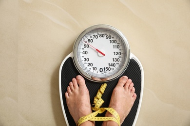 Photo of Woman with tape standing on floor scales indoors, top view. Overweight problem