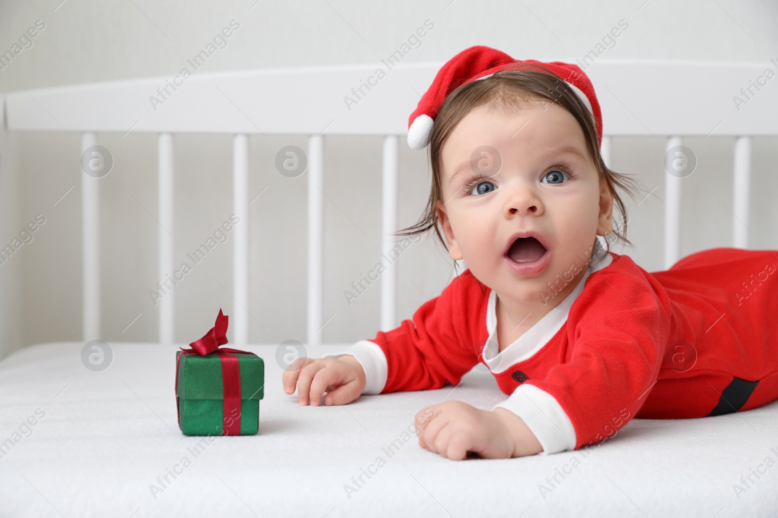 Photo of Cute baby wearing festive Christmas costume with gift box in crib