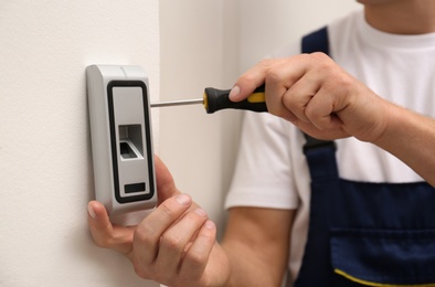 Photo of Male technician installing fingerprint security alarm system indoors, closeup