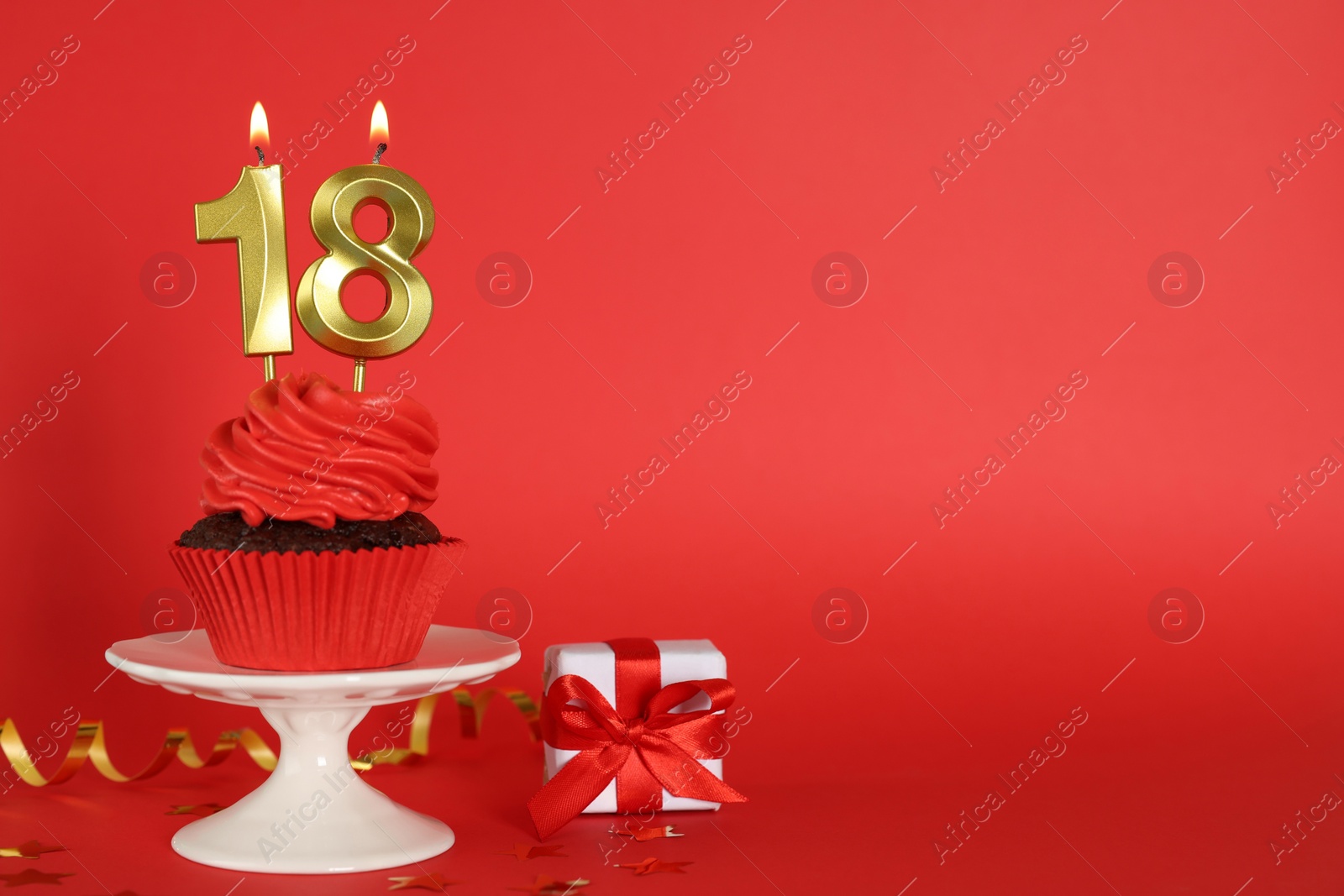 Photo of Delicious cupcake with number shaped candles on red background, space for text. Coming of age party - 18th birthday