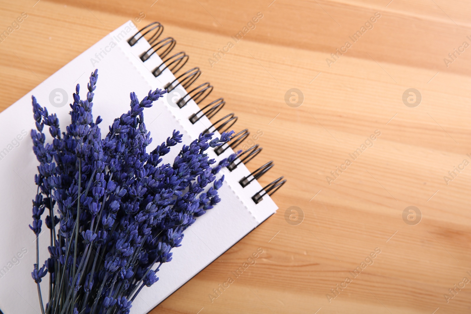 Photo of Bouquet of beautiful preserved lavender flowers and notebook on wooden table, top view. Space for text