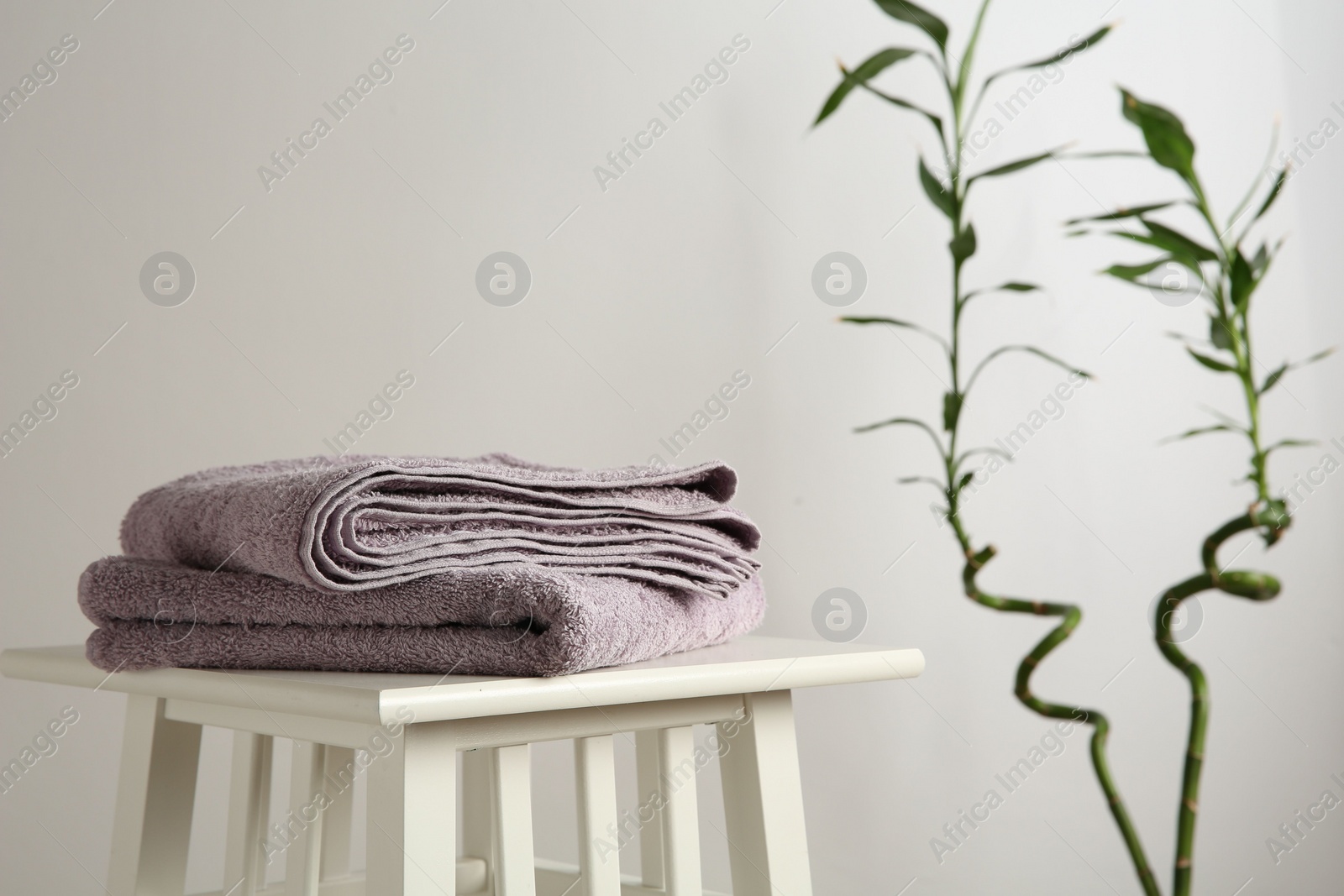 Photo of Violet towels on stool against white wall. Space for text