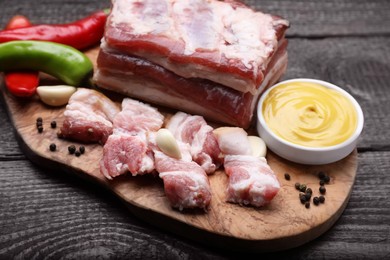 Photo of Pieces of pork fatback with chilli pepper and sauce on wooden table, closeup