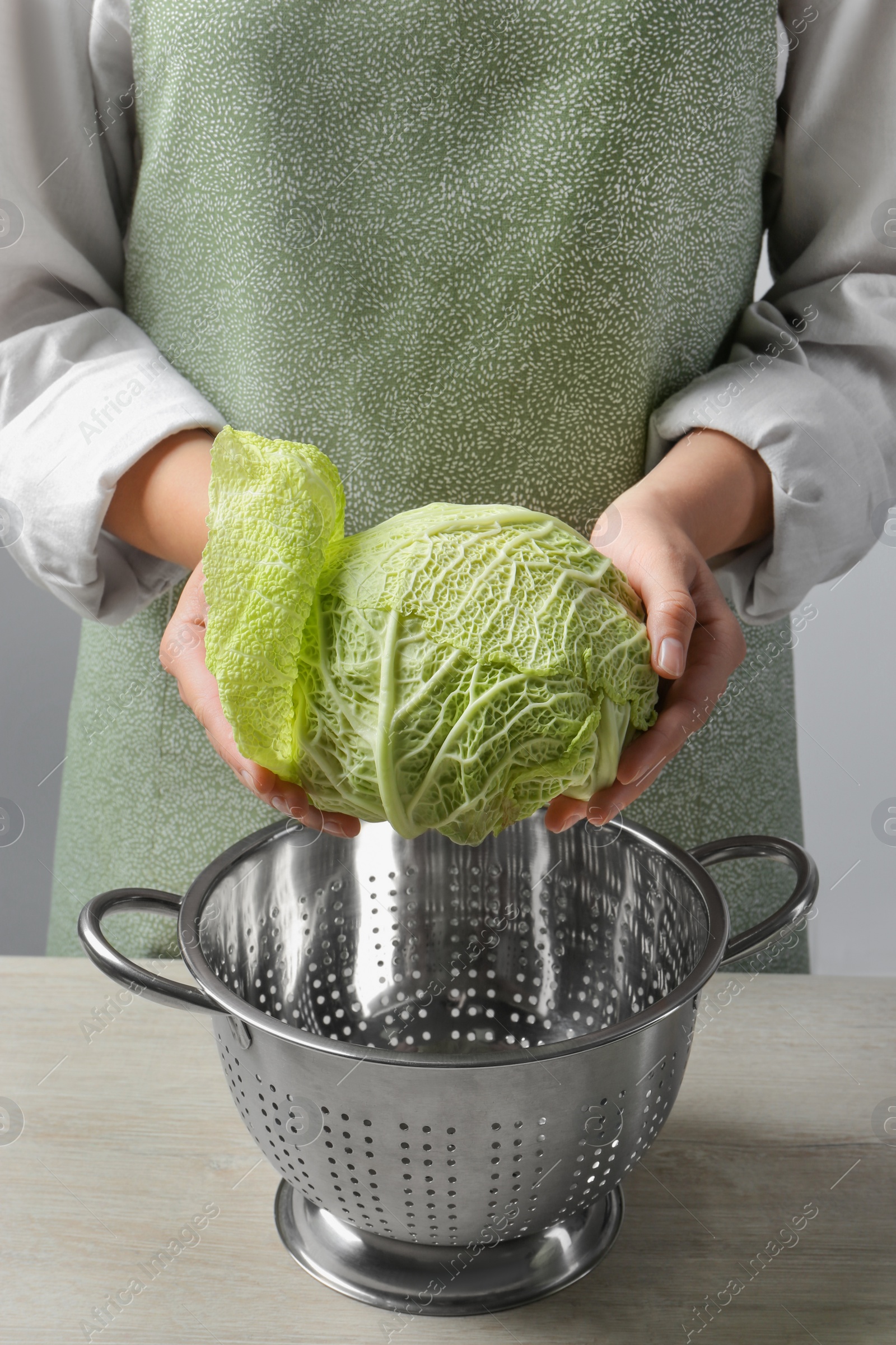 Photo of Woman separate leaf from fresh savoy cabbage at wooden table, closeup