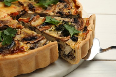 Delicious quiche with mushrooms and spatula on white wooden table, closeup