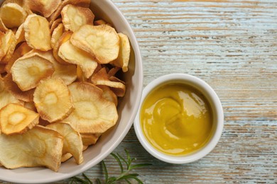 Photo of Tasty homemade parsnip chips with sauce and rosemary on old light blue wooden table, flat lay. Space for text