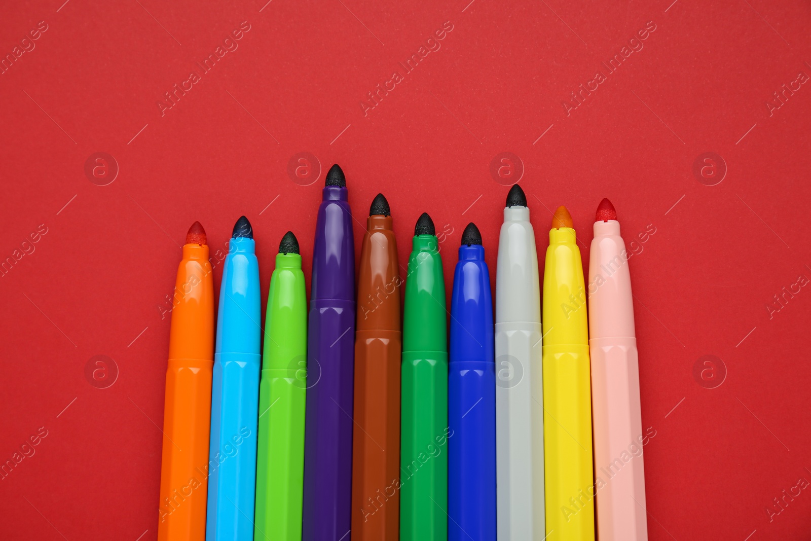 Photo of Different colorful markers on red background, flat lay. Space for text