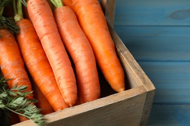 Photo of Fresh ripe juicy carrots in basket on light blue wooden table, closeup. Space for text