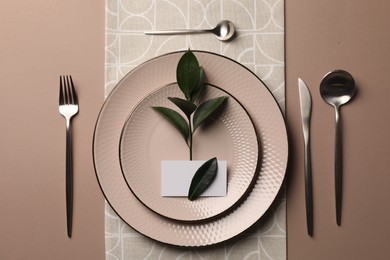 Stylish table setting. Plates, cutlery, blank card and green twig on beige background, flat lay