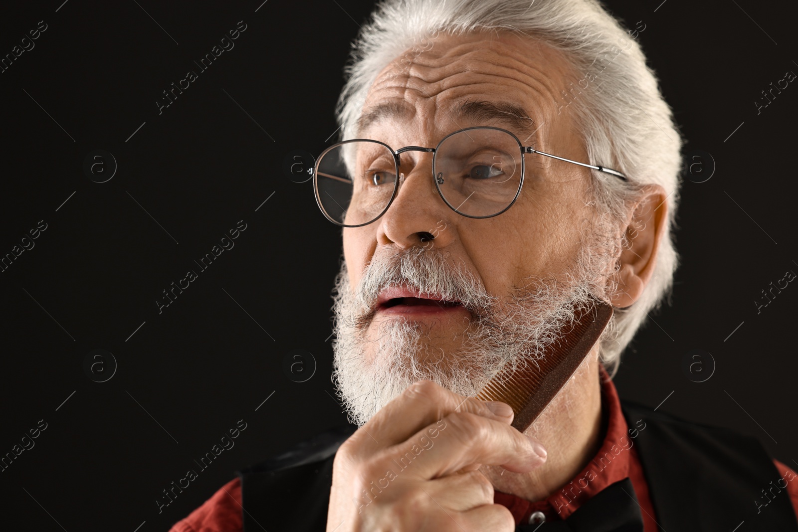 Photo of Senior man combing mustache on black background, space for text