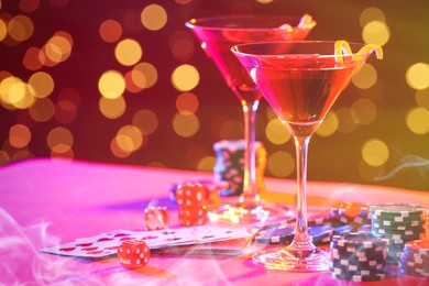 Image of Cocktail, dice, playing cards and casino chips on table against blurred lights. Bokeh effect
