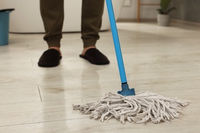 Photo of Man cleaning floor with mop indoors, closeup