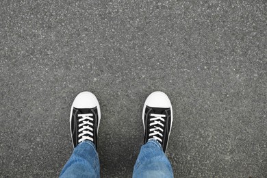 Man in sneakers standing on asphalt, top view. Space for text