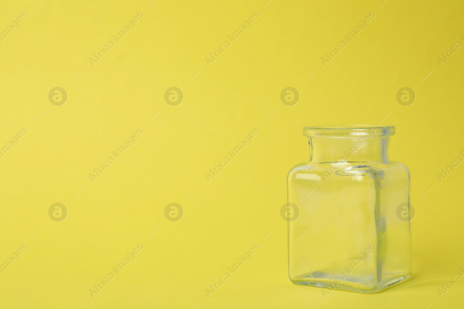 Photo of Open empty glass jar on light yellow background, space for text