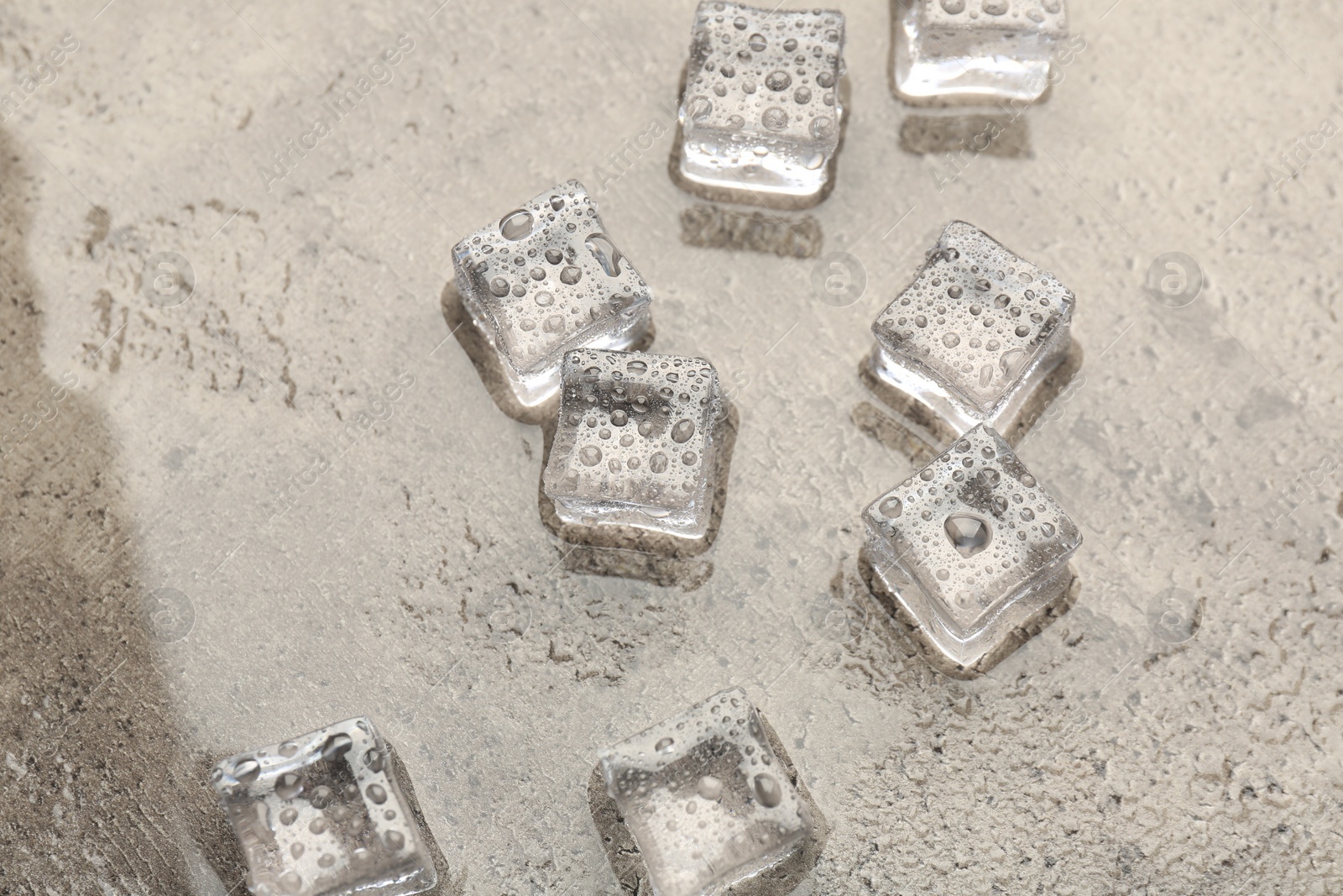 Photo of Melting ice cubes and water drops on grey textured table, above view