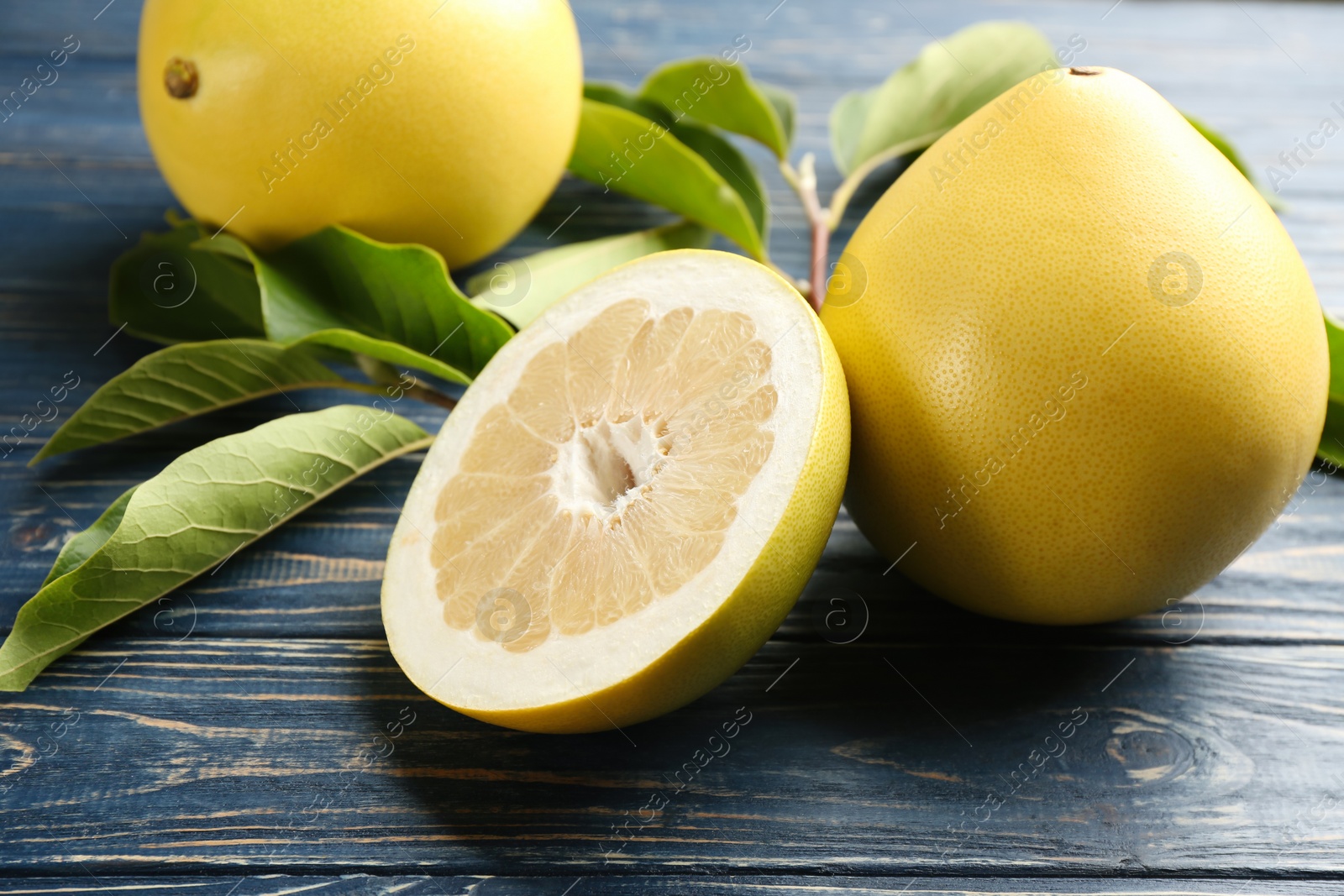 Photo of Fresh cut and whole pomelo fruits on blue wooden table, closeup