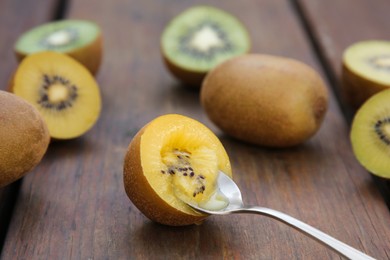 Photo of Spoon with half of kiwi and fruits on wooden table, closeup