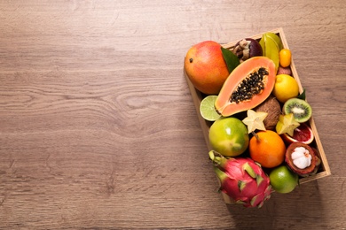 Photo of Different tropical fruits in box on wooden table, top view. Space for text