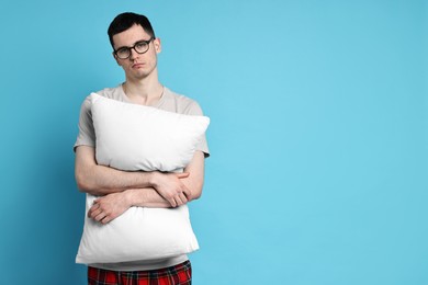 Man in pyjama holding pillow on light blue background, space for text