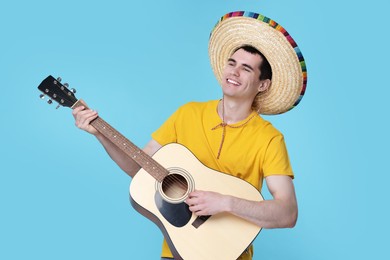 Photo of Young man in Mexican sombrero hat playing guitar on light blue background