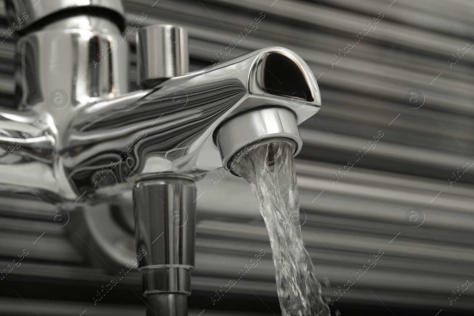 Photo of Water flowing from bath tap on blurred background, closeup