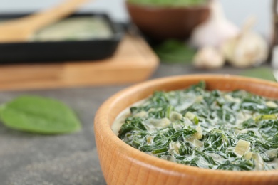 Photo of Tasty spinach dip in wooden bowl on grey table, closeup