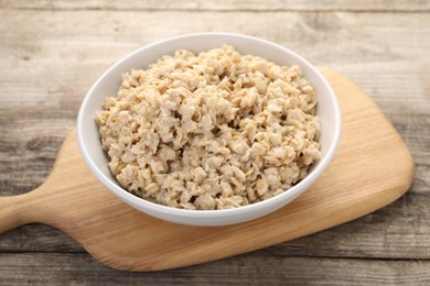 Photo of Tasty boiled oatmeal in bowl on wooden table, closeup