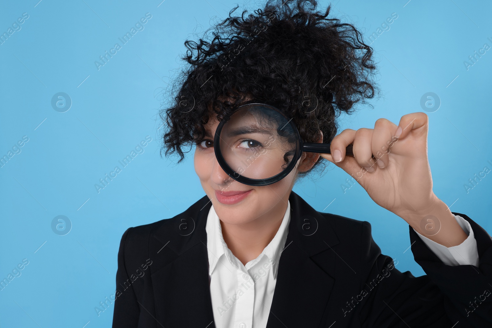 Photo of Curious young woman looking through magnifier glass on light blue background