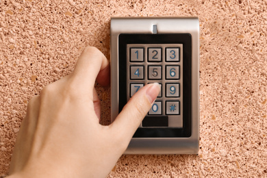 Photo of Woman entering code on electronic lock's keypad indoors, closeup