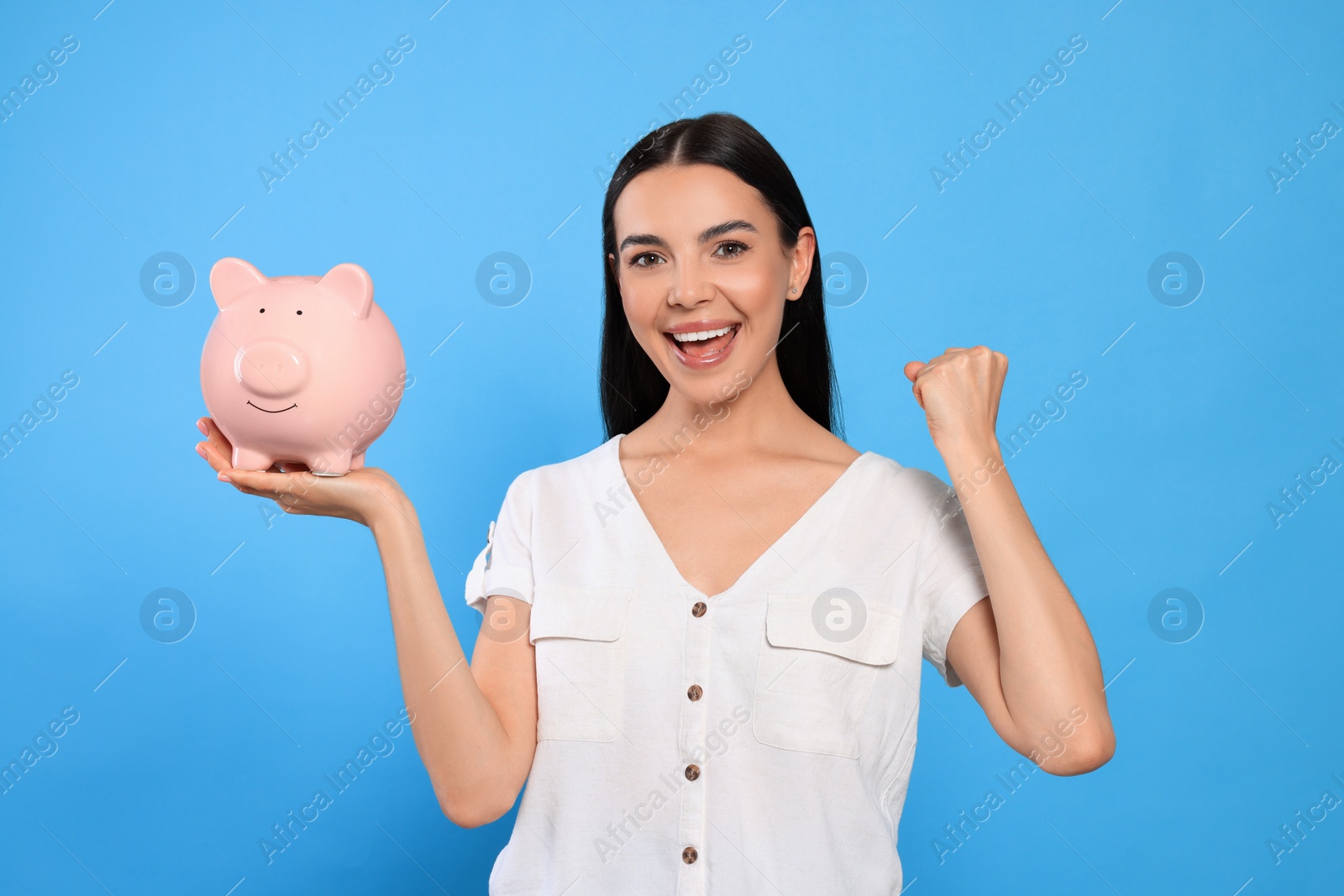 Photo of Emotional young woman with piggy bank on light blue background