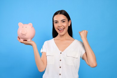 Photo of Emotional young woman with piggy bank on light blue background