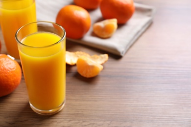 Photo of Glasses of fresh tangerine juice and fruits on wooden table, space for text
