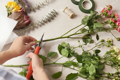 Photo of Female florist pruning stem at table, top view