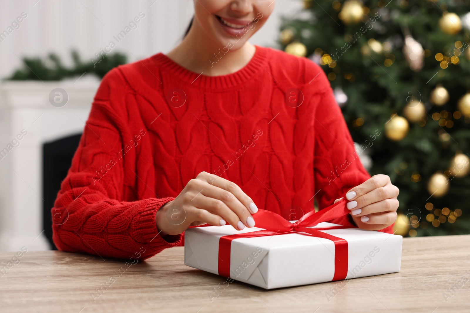 Photo of Woman opening Christmas gift at wooden table in room, closeup